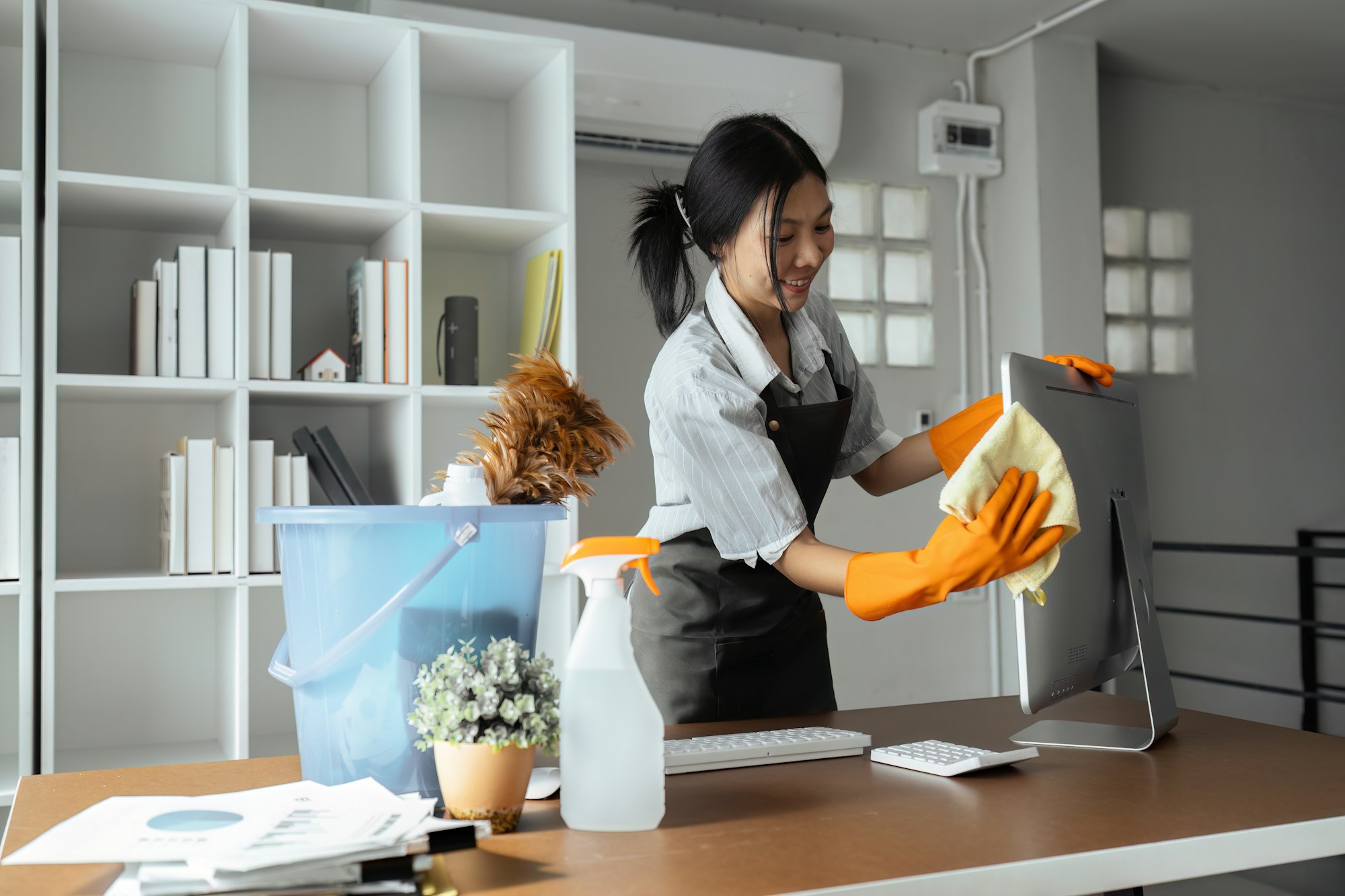 Woman maid cleaning and wiping the computer with microfiber cloth in office